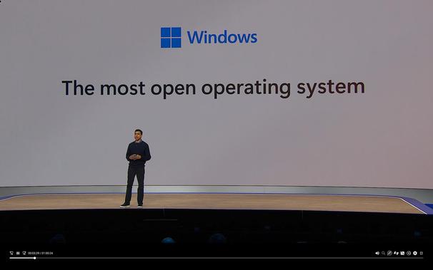 A screenshot of Microsoft's keynote, with a person in front of a giant screen that says "Windows, the most open operating system"