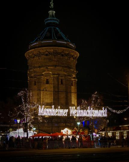 Blick auf den Weihnachtsmarkt am Mannheimer Wasserturm. Im Hintergrund zu sehen ist der beleuchtete Wasserturm.