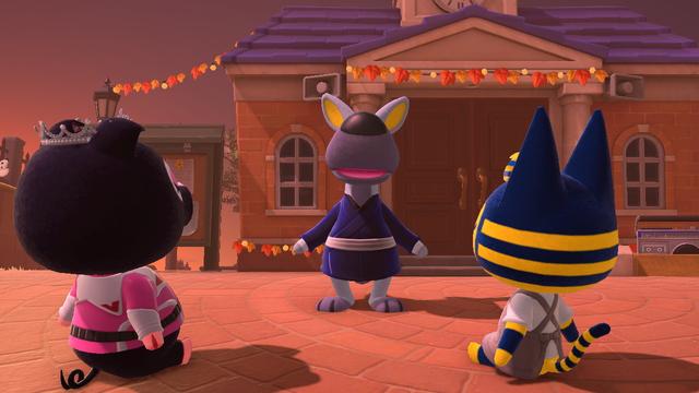 Animal Crossing: New Horizons screenshot. Set in the town square with building decorated with leaves for Thanksgiving. Sitting on the brick town square are Agnes and Ankha seen from behind. In front of them is Walt (grey kangaroo) who is speaking to them. What is he telling them?