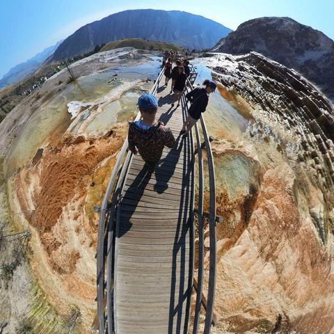 Photo of people walking on a boardwalk over a hot springs area in Yellowstone National Park.