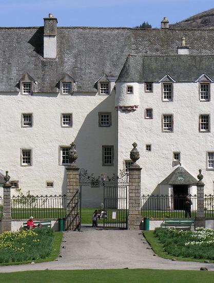 Today's 'Where in Scotland' image. It is a vertical image showing a view of a section of a large white castle set beyond ornate railings and a gate that is half open. There is a drive and lawn at the foot of the frame. The castle is four storeys high and has grey slate roofs and extends out of both sides of the frame. The sky is blue.