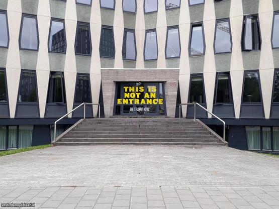 Datum opname: augustus 2019. De in onbruik geraakte hoofdingang aan de Jan van Galenstraat. De ramen hebben geen normale scharnieren maar draaien om assen (taatsen) in het midden van de kozijnen.
