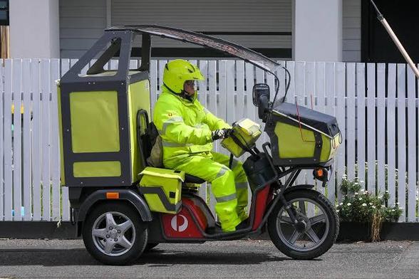 A postie riding an Australia Post electric trike. Lots of yellow! The postie even has a yellow helmet and yellow hi viz overalls.