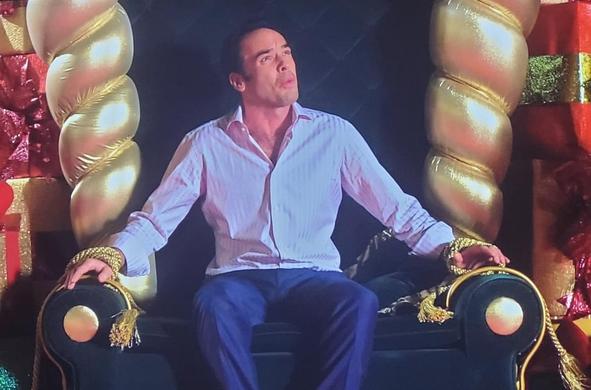 Paul Blackthorne (an Anglo Saxon man in his 30s) sitting on a mall Santa throne looking up confused. His arms are tied to the chair with gold cord.