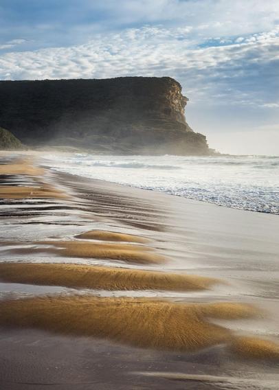 a vertical seascape with the cliff in background. The foreground is made of alternating sections of sand and water making a pleasing repetition.