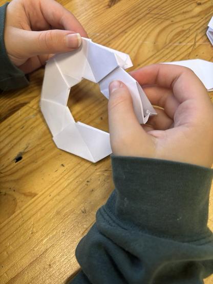 Das Bild zeigt zwei Kinderhände, die einen weißen Papierstern falten.