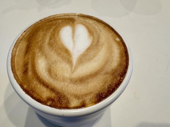 Close up of a small white coffee mug filled with a cappuccino sitting on a white table.