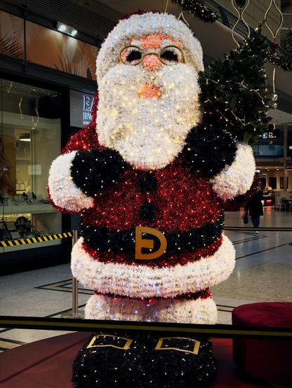 Alt Text by @altbot@fuzzies.wtf

Deutsche Version:

Eine große, festliche Weihnachtsmannfigur steht in einem Einkaufszentrum. Der Weihnachtsmann besteht aus rot-weißem Lametta, wird mit kleinen Lichtern beleuchtet und hält einen kleinen Weihnachtsbaum. Er trägt eine Brille und hat einen großen, flauschigen weißen Bart. Ein goldener Buchstabe "D" ist auf seinem Gürtel zu sehen. Der Boden ist glänzend und ein Teil des Schaufensters eines Ladens ist im Hintergrund sichtbar.

English Version:
A large, festive Santa Claus figure stands in a shopping mall. The Santa is constructed of red and white tinsel, illuminated with small lights, and holds a small Christmas tree. He wears glasses and has a large, fluffy white beard. A gold letter "D" is visible on his belt. The floor is shiny, and a portion of a store's display window is visible in the background.