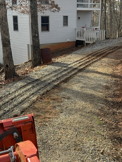 A gravel driveway in front of a house with four grooves scraped in it from a tractor.