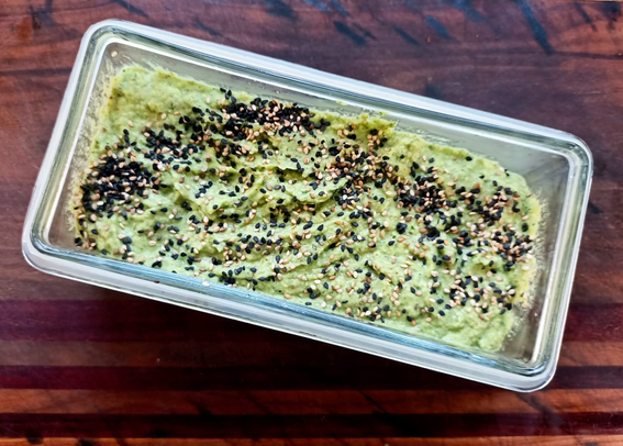 in einer viereckigen Glasschale eine hellgrüne Creme mit schwarzen und weißen Sesamkörnern bestreut.