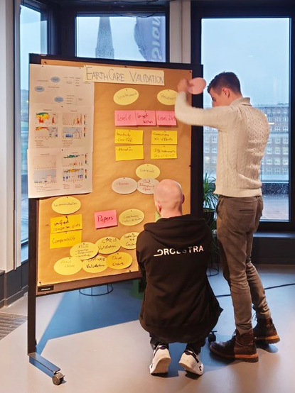 Two scientists are pinning notes onto a board, which is overwritten with "EarthCARE validation".