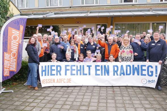 Die Teilnehmer:innen des HessenForums vor dem Eingang zur Jugendherberge. Alle halten Postkarten für den Fahrradklima-Test hoch und halten vor der Gruppe ein Banner HIER FEHLT EIN RADWEG! Heesn.adfc.de

 © Dr. Anja Wagner