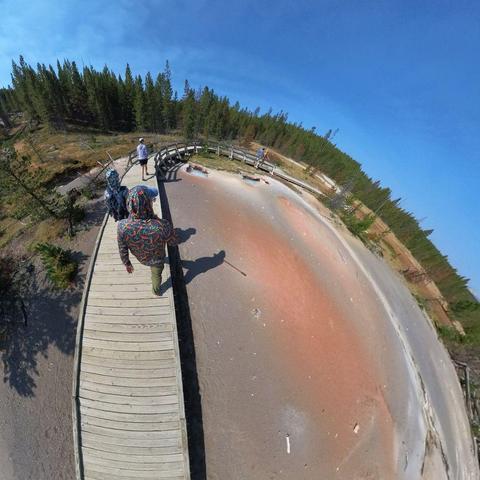 Photo of three people walking on a boardwalk over a hot springs area in Yellowstone National Park.