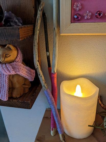 Three homemade wooden wands on my mantelpiece, next to an LED candle. The lavender wand is pale, gnarled and twisty; the Fuchisa wand is very pale and almost straight; the Beech wand is thinner than the other two, slightly bent, and has its dark brown bark left on.