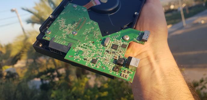 I'm holding up the innards of a broken external hard drive. The drive still has its control board attached. In the bottom right corner of the board a very unhappy looking power step-down converter IC can be seen.