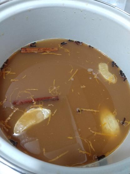 A kettle with a gallon of fresh cider in it, with cinnamon sticks, cloves, orange rind, and orange peels flavoring it, heated to just slightly below simmering.