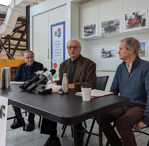 Trois hommes assis à une table devant des micros de presse. Derrière eux, un mur blanc où l'on peut voir des photos de moyens de transports anciens.