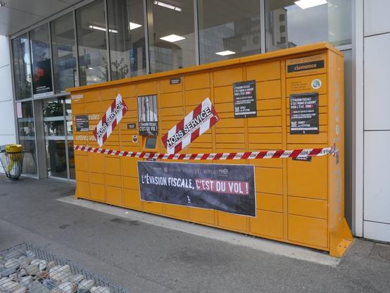 Consigne automatique de colis d'Amazon (Amazon locker) décoré avec des affiches et des stickers dénonçant l'évasion fiscale d'Amazon.