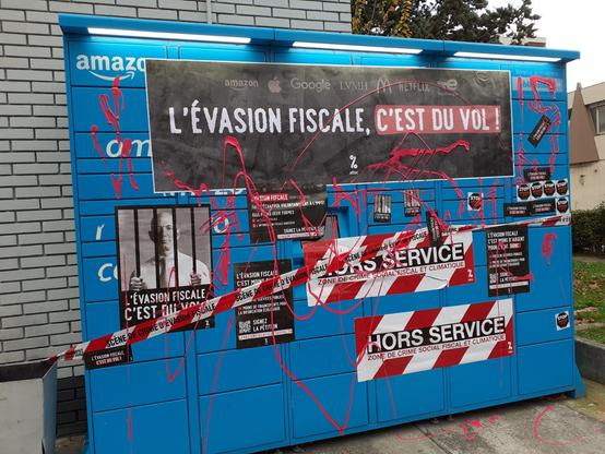 Consigne automatique de colis d'Amazon (Amazon locker) décoré avec des affiches, des stickers et aspergé de gouache pour dénoncer l'évasion fiscale d'Amazon.