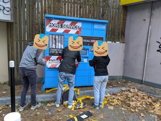 Trois activistes devant une consigne automatique de colis d'Amazon (Amazon locker), en train de coller des affiches et des stickers pour dénoncer l'évasion fiscale d'Amazon.