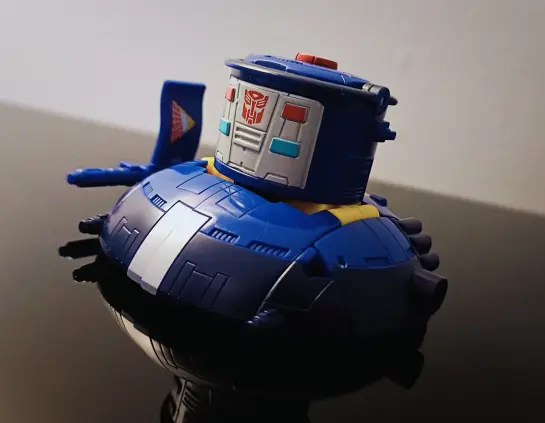 Pathfinder in UFO alt-mode. Mostly blue with a black 'rim' (oo-er) and a facing panel on the pot in metallic grey with various colourful details including the autobot logo. Attached to the left side is the flag stroke gun weapon that comes with the figure.