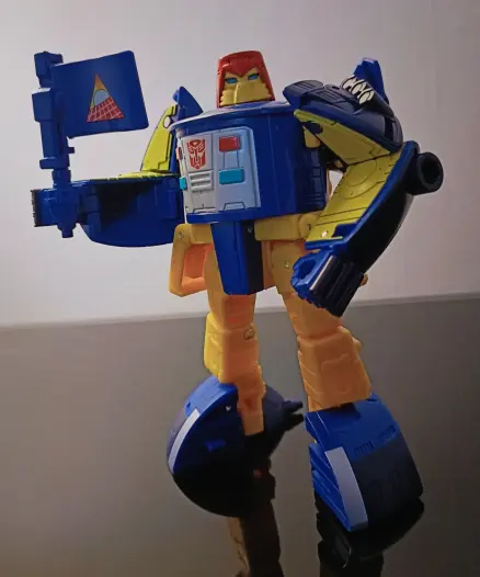 Pathfinder converted into Robot mode, now holding the weapon as a flag. Conversion introduced a lot of yellow into the figure, on facing arm panels and legs and hip-plates. The head is a red fez-like shape with a yellow face-plate and striking blue eyes. The black has receded leaving blue and yellow as the colour scheme. Neat trick. She's tubby in this mode but that just makes her more adorable.