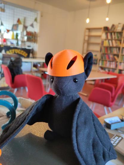 Ich, der hübsche ft1, probiere wie der Fahrradhelm-Protoyp passt.
Er passt nicht ganz so gut, aber immerhin sind die Aussparungen für meine schönen Ohren an der richtigen Stelle.
Ich sitze auf einer Metallplatte und im Hintergrund sind ein Tisch mit Sesseln und ein Bücherregal zu erkennen. Dazu noch ein "Refugees Welcome"-Transparent.