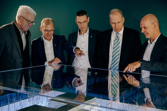 Ministerpräsident Winfried Kretschmann (links) steht mit vier weiteren Männern im Halbkreis um einen Glaskasten und betrachtet das darin aufgebaute Modell des Umspannwerks. © Staatsministerium BW | Ilkay Karakurt