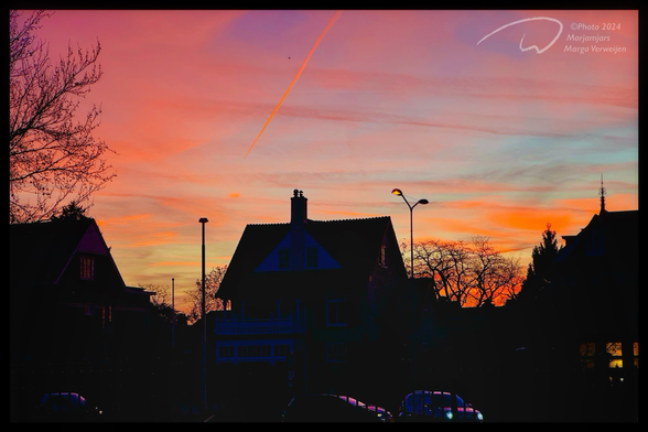 Silhouettes of houses and trees against a sunset sky, a plane leaving a trail behind.