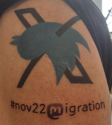 Photo of a tattoo on shoulder: dead twitter Bird on its back impaled with the X logo with hashtag nov22-Mastodon logo as "M"-igration