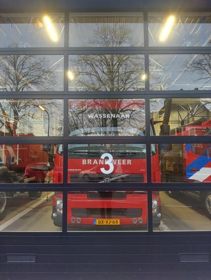 Foto van een rode brandweerauto door de glazen deur van de brandweerkazerne ¦ Photo of a red firetruck through the glass door of the fire station