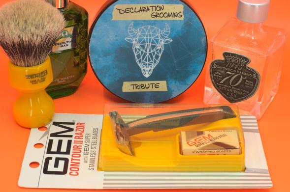 A GEM Contour II in its original packaging in front of a tub of DG Tribute, a bottle of SV 70ᵗʰ splash, Stirling Executive Man frag and a beautiful butterscotch Zenith badger brush