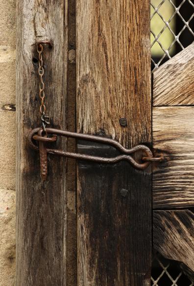 a photo of an old latch on a wooden door frame, the wood is weathered and the metal latch is rusty and ramshackle