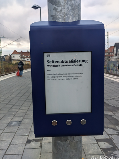 Anzeigetafel an Bahnhof "Seitenaktualisierung. Wir bitten um etwas Geduld" auf was aussieht wie Papier, unten drei Knöpfe. Ich vermute eInk-Display.