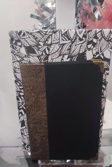an a6 single signature pamphlet, with black faux leather as cover, and on the side decorated copper color faux leather. in front of a bigger hardcover  with a pattern of black and white leaves.