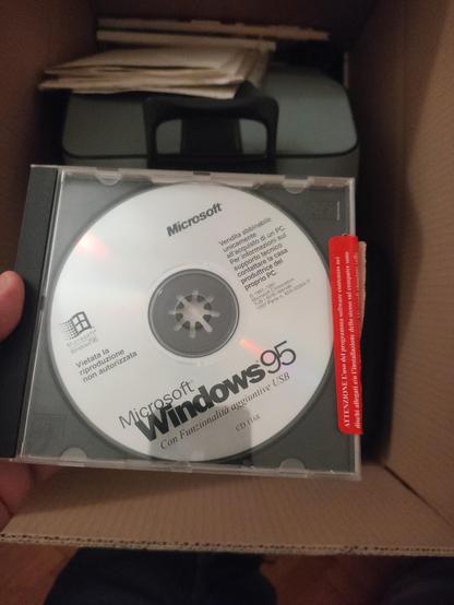 Foto di un CDROM di Windows 95 nella sua custodia. Sullo sfondo uno scatolone di reperti dalla casa in cui sono cresciuto.