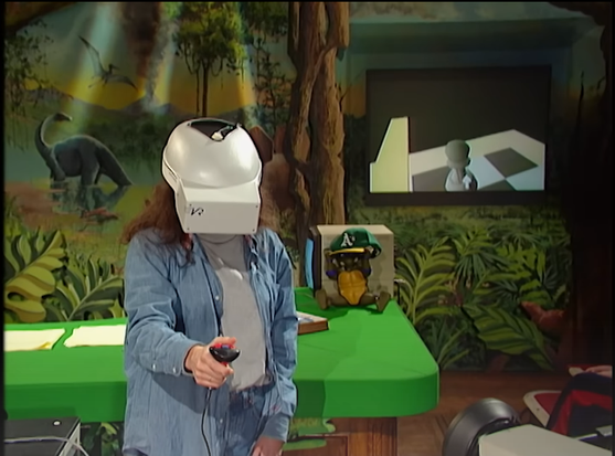 Uma garota de cabelos longos e camisa manga longa aberta, segurando um joystick com fio que lembra o atual Wiimote, com um capacete de realidade virtual. Ao fundo, uma ilustração de um dinossauro e uma TV, exibindo o que ela vê, um tabuleiro de xadrez e um peão sendo movimentado nele.