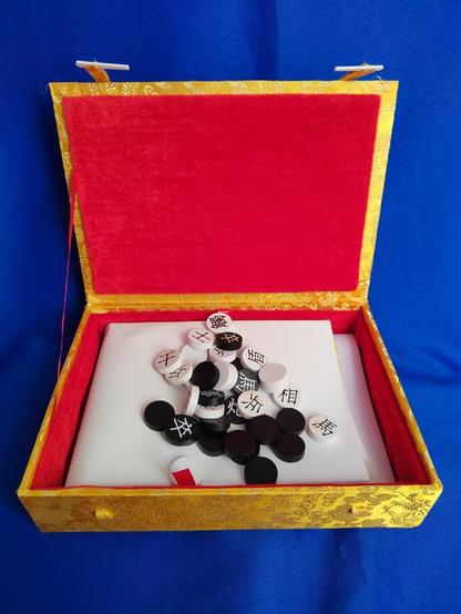 The components inside are very much the product of small-press self-publication: a thick glossy stock paper board with small round pieces with the characters for the pieces on one side.  Half are black, half are white.