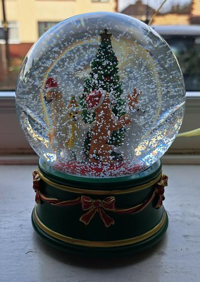 A swirling snow globe. The globe contains a Christmas tree around which four dogs on their hind legs appear to be dancing a conga. The dogs are all different breeds. Three of them are wearing red festive hats, and the front one is wearing antlers. A rainbow can faintly be seen at the top of the globe as the sunlight reflected off the house opposite refracts through the liquid.
This snow globe was chosen by my granddaughter last year as she is obsessed with dogs.
