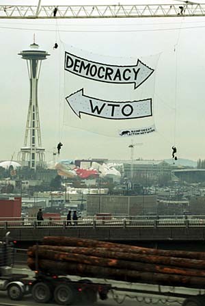 29 Nov99-Seattle,WA: Five activists from the Rainforest Action Network climbed a giant crane and unfurled a 2000 square foot banner just before dawn today, protesting the World Trade Organization’s anti-democratic policies. The action marked the first day of the WTO ministerial meetings. “Using a celluar phone to talk to the press while hanging from the crane, climber John Sellers said: “The WTO is a threat to democracy and our hard-one environmental, labor, health and safety laws and must be abolished.” The activists remained high over the Seattle skyline until just past noon when they voluntarily surrendered to the Seattle police. All five climbers plus one support person were arrested.