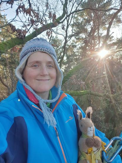 Selfie ich bin im hinter mir scheint die Sonne ich habe ein Eichhörnchen Plüschtier dabei ich trage eine blaue Jacke und blaue Mütze