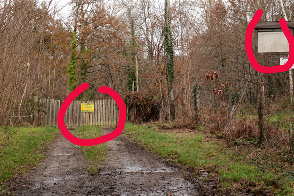 Un chemin boueux avec un panneau effacé sur une potence à droite (entouré de rouge sur l'image) . Au bout de quelques mètres, un portail fermé bloqué l'accès et un panneau vert et jaune est posé (il est entouré en rouge sur l'image). Le texte trop petit pour la photo indique "chasseurs et promeneurs, respectons nous"