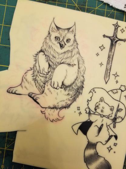 Photo of some fake skin with some tattoos that I've done on it. It shows a fluffy owlbear, a doodle of a sword, and a raccoon mage.