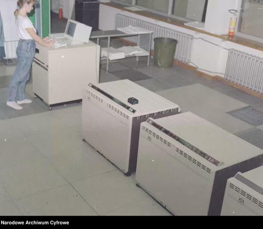 ICL Series 39 Level 35 computers. In the background a girl at a terminal with a keyboard and monitor. Halon fire extinguishers are also visible.

Dates: 1985 - 1990
Photographer: No data
Negative number: 53-5164
Upload: Arkadiusz Sikorski / https://arq.pl/