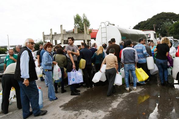 Molta gente con bottiglie e bidoncini in mano si affolla attorno a un'autobotte per la distribuzione dell'acqua.