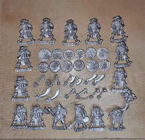 A set of unpainted orc miniatures arranged on a table includes various figures: troopers, a leader, a standard bearer, and a musician, all ready for painting and assembly.