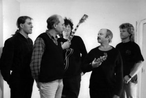 In Cahoots quintet - black and white landscape format - standing in a close group, Phil centre rear (grinning and wearing his guitar), Hugh and Elton (cradling his sax) apparently in conversation, bracketed by Steve and Pip looking on