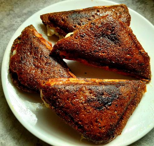 Four dark brown grilled sandwich triangles on a white plate.