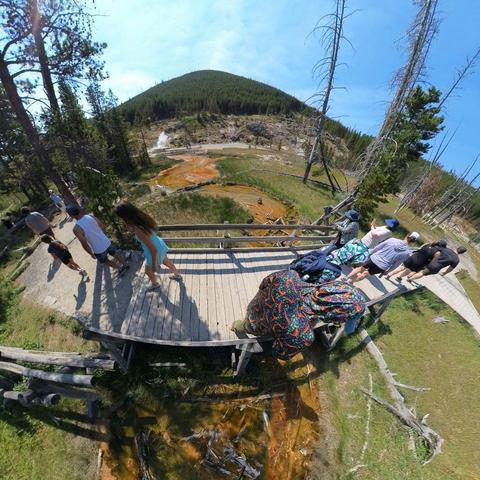 Photo of people walking on a boardwalk over a hot springs area in Yellowstone National Park.