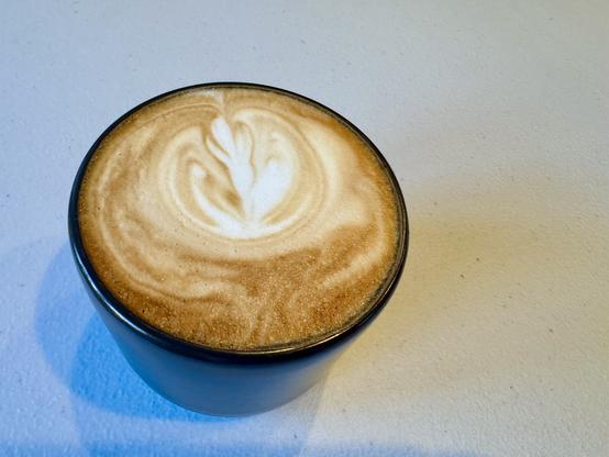 Small black coffee mug filled with a frothy cappuccino sitting on a gray white textured table.